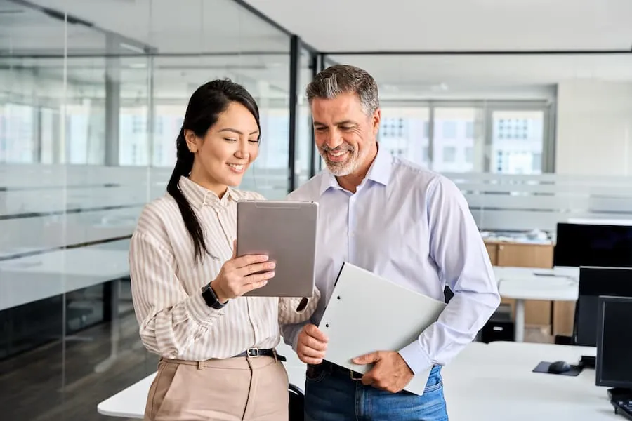 Two colleagues smiling while reviewing a document on a tablet