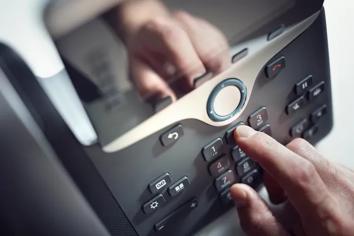 A hand dialing an old office desk phone